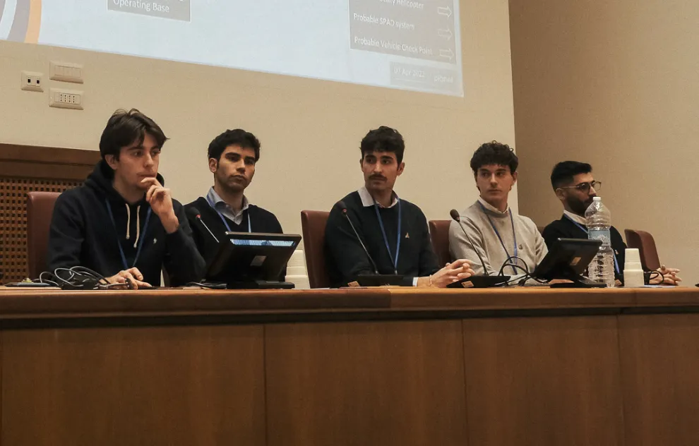 Five team members at a panel table with microphones during the CASSINI Hackathon.